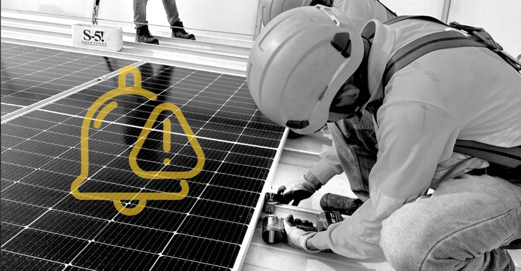 A worker installing solar panels, wearing a helmet and using a drill, showcasing renewable energy technology.